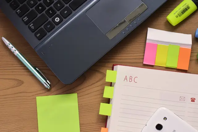 A work desk with a laptop, a notebook, sticky notes and a phone